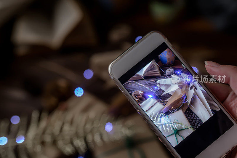 手机在一个博主手里。为博客摄影的过程包装工艺礼物的圣诞节和纸星星从袋子。