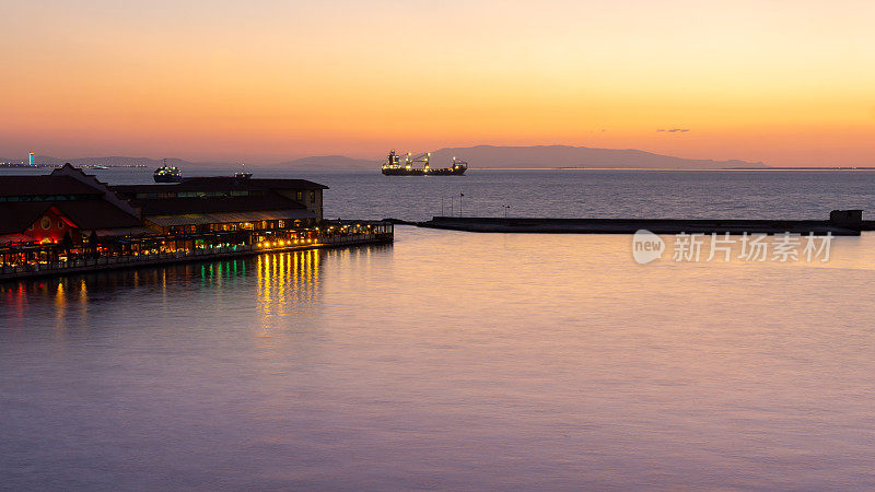 土耳其伊兹密尔港日落时的风景，船的剪影航行，背景是水平格式的山脉。