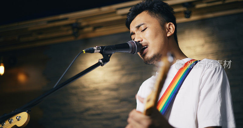 年轻的亚洲男性音乐家穿着休闲服，在歌手唱歌的同时弹着电吉他