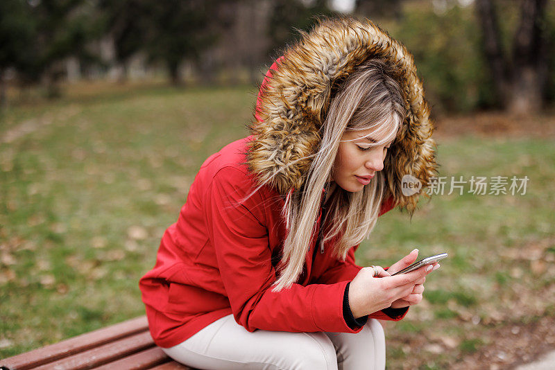 微笑的年轻女子坐在公园的长椅上发短信