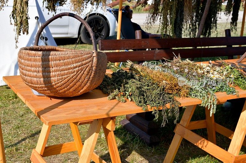 在波兰中世纪的节日里，一个布制帐篷里的木桌上有一个柳条篮子，旁边放着一些干药草、鲜花和其他种类的花絮