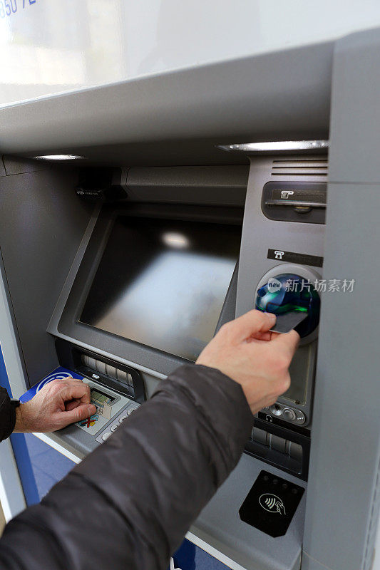 一名男性银行顾客使用借记卡和信用卡通过自动柜员机完成交易的垂直镜头