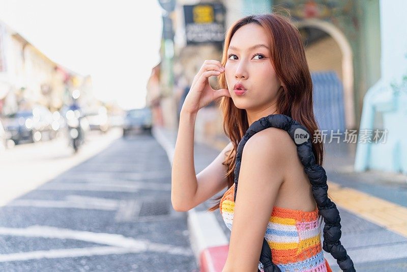 这位Z世代亚洲女性在普吉岛老城的路边摆出可爱的姿势，在她的旅行冒险中享受着放松的时刻