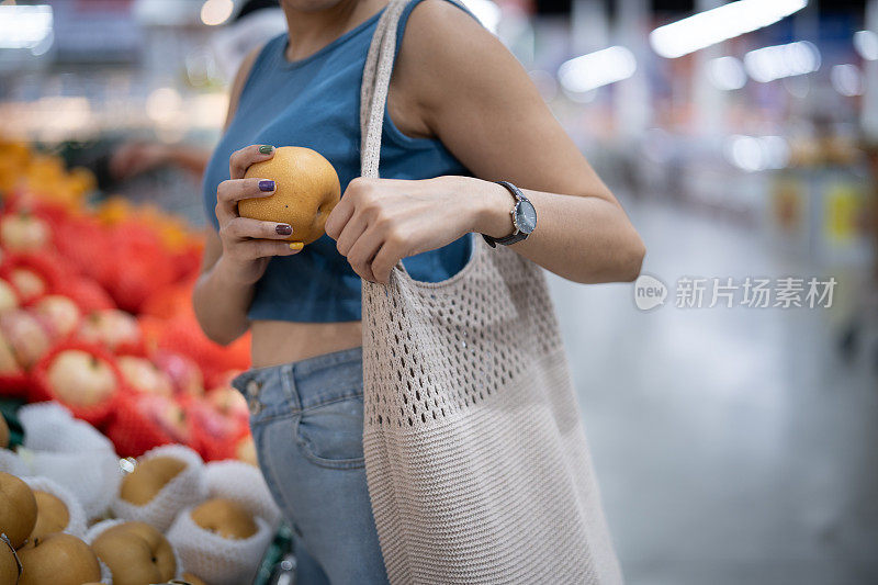 年轻的亚洲妇女在商场用布袋买水果，可重复使用的容器和可持续的环保概念。