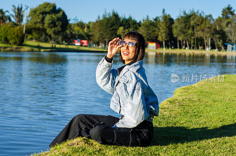 在一个阳光明媚的日子里，一名剪短头发的年轻女子在公园里穿着休闲服，戴着太阳镜