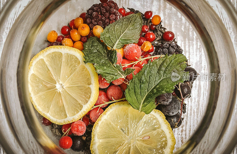 五颜六色的水果茶在一个玻璃茶壶与新鲜水果片-柠檬，红莓，沙棘，黑莓，新鲜冷冻浆果与蜂蜜和芳香的茶，芳香的饮料与维生素