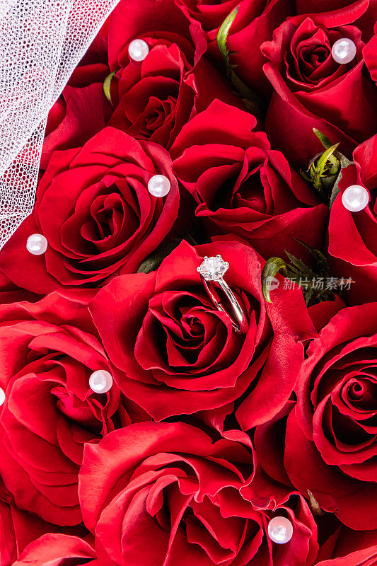 一个别致的白金订婚戒指与红色活玫瑰和珍珠的背景。明信片、邀请函、封面的模型。婚礼设计。俯视图