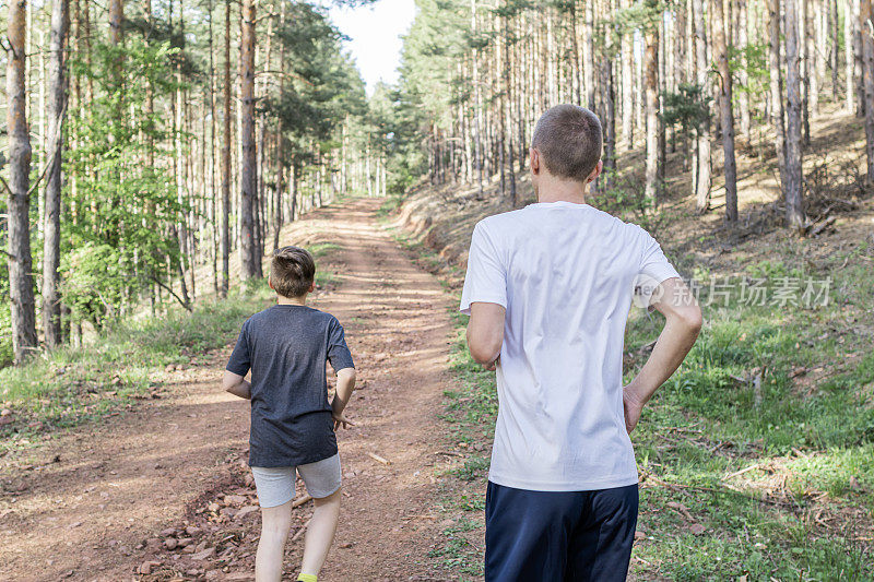 快乐的父亲和儿子正在森林里跑步和锻炼。他们在外面伸伸懒腰，一起享受。运动的生活方式。