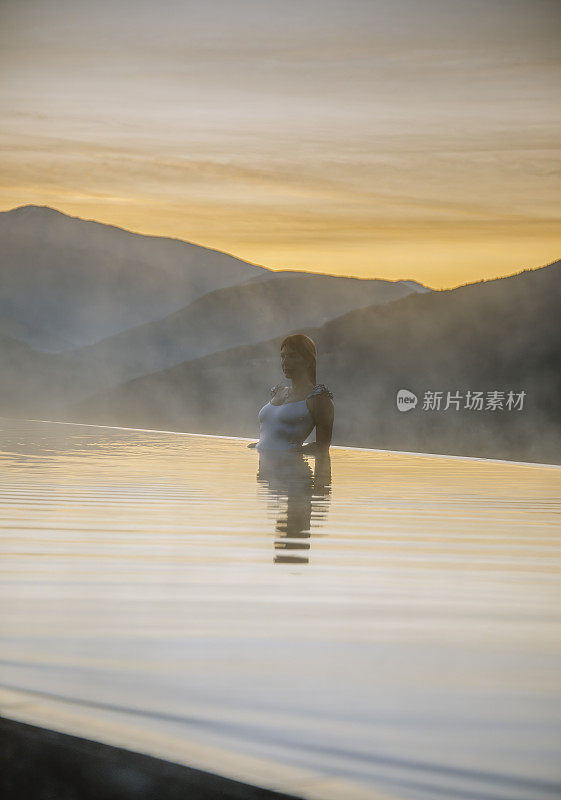 在意大利的多洛米蒂，一名年轻女子站在无边泳池边，欣赏日落美景，并在泳池边放松，欣赏自然景观