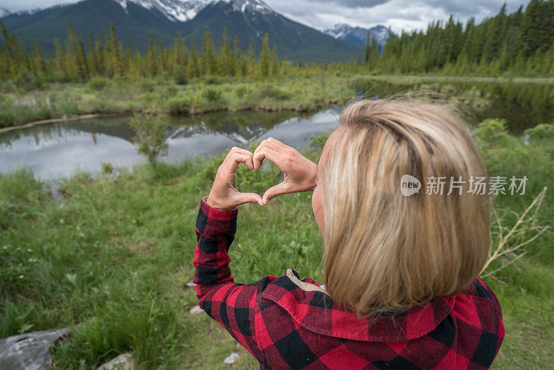 年轻女子在山湖上做心形手指架