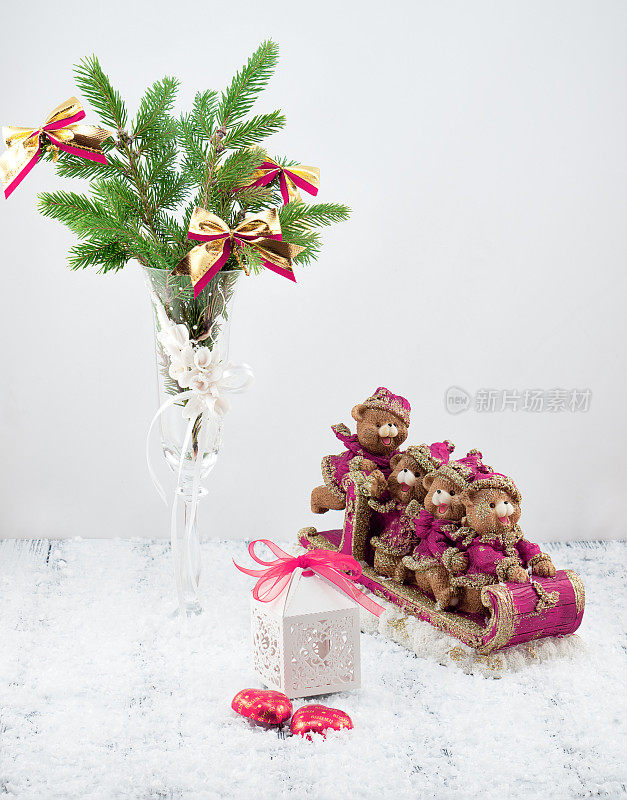 白色装饰的圣诞树，白色的礼盒，粉色和棕色的玩具熊在雪橇上，糖果和雪在复古的白色桌子上在白色的背景