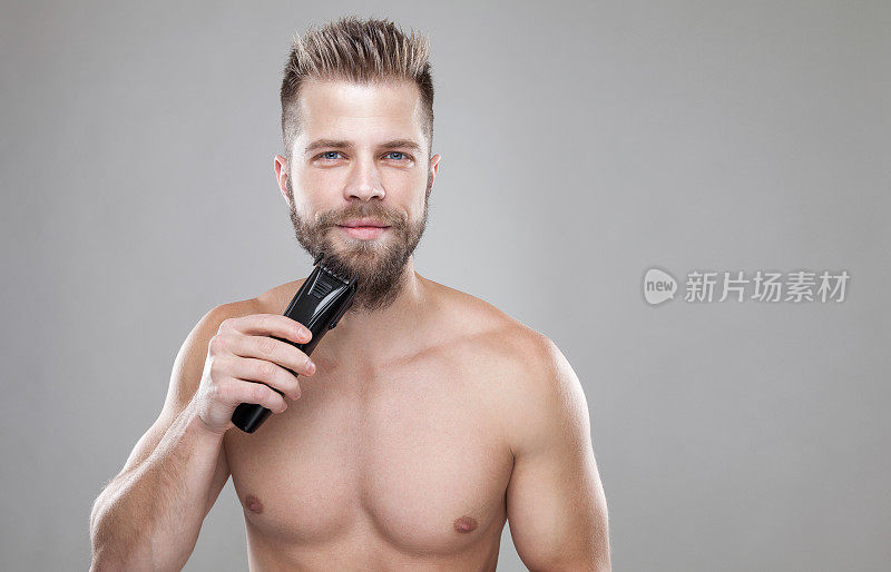 英俊的蓄胡须的男人正在用修胡子机修胡子