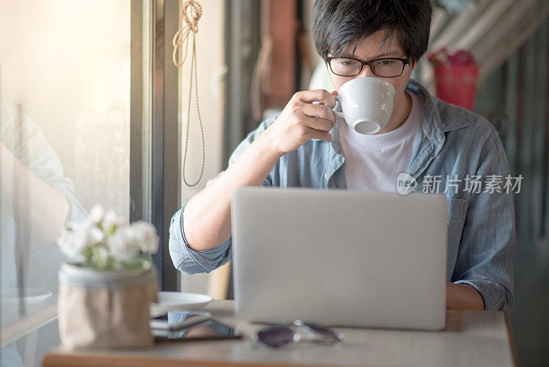 年轻的亚洲快乐的男人使用笔记本电脑在咖啡馆的咖啡时间