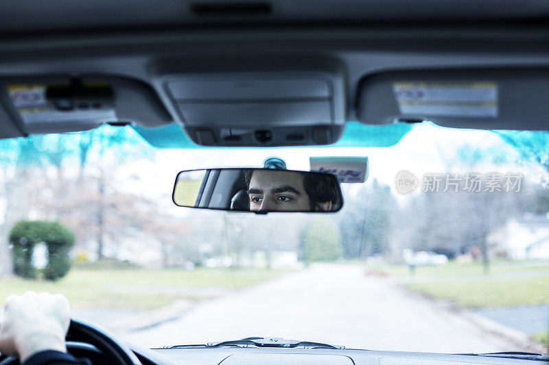 年轻的大学生司机反映在汽车内饰镜