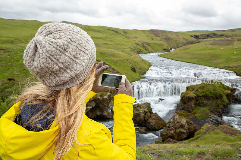 一名年轻女子在冰岛瀑布边用手机拍照