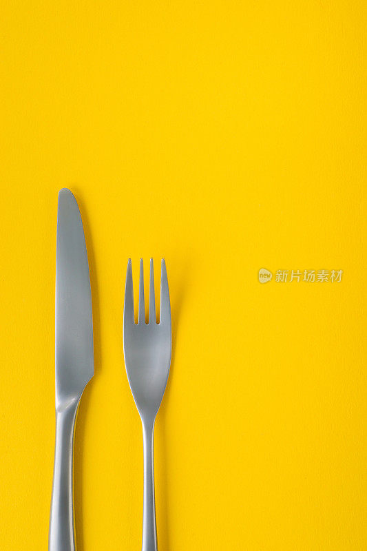 叉和刀在黄色背景上，稀疏的构图与复制空间。