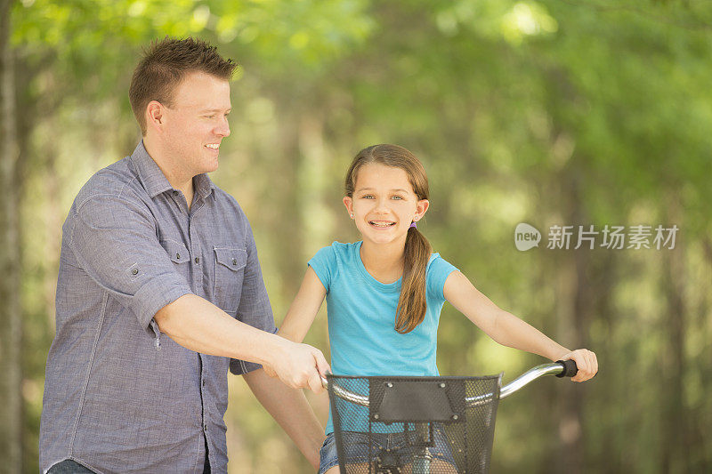 和爸爸一起骑自行车。小女孩，爸爸在外面。院子里。夏天。