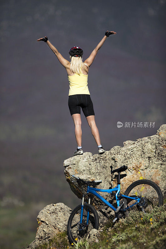 金发女性在山岩上庆祝自行车爬到山顶