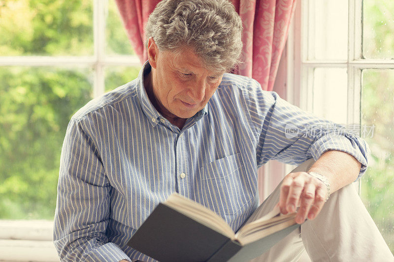 一个成熟的男人坐在他的凸窗边看书