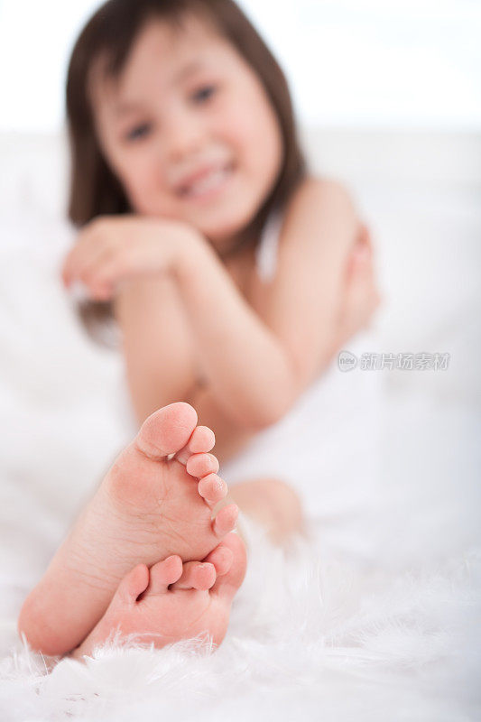 小女孩微笑着在床上玩羽毛