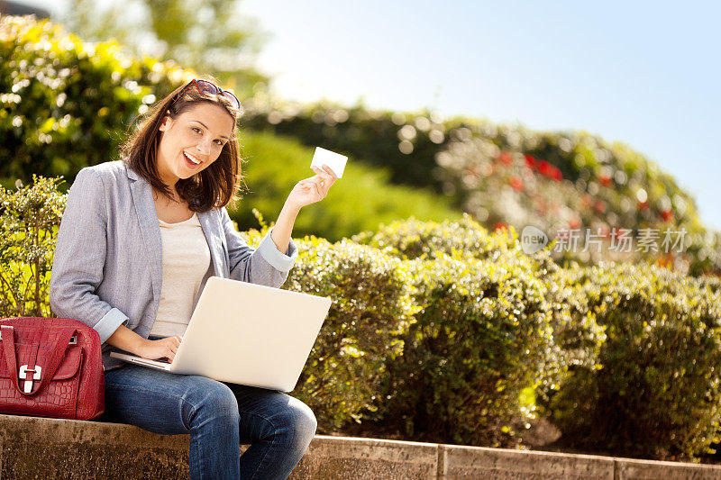 年轻女子坐在户外，拿着笔记本电脑和卡片