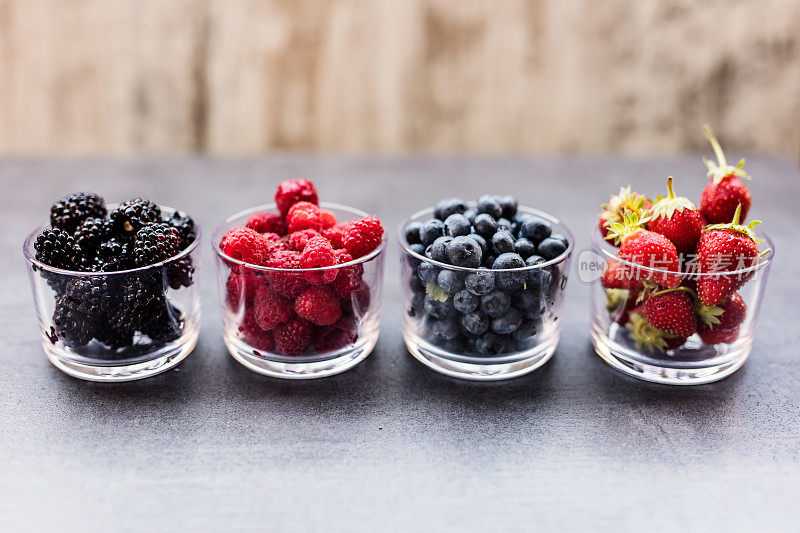 四个盛满夏季浆果的碗，比如草莓、覆盆子、蓝莓和黑莓。