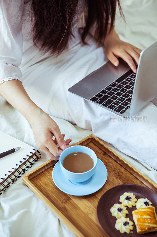 一个女人在床上用笔记本电脑喝咖啡