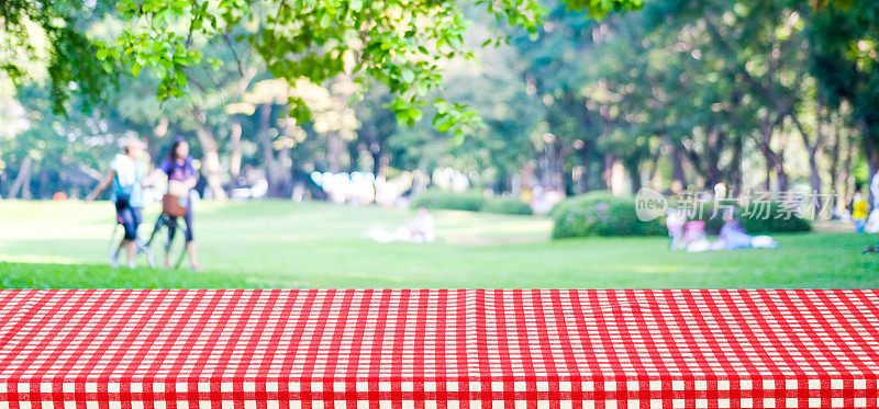 空桌子覆盖红色桌布模糊公园与人的背景，为产品展示蒙太奇背景，横幅
