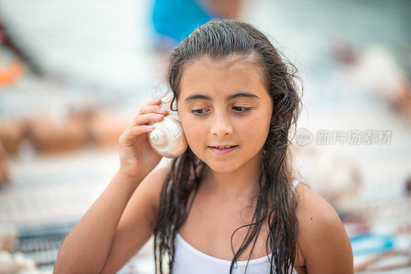 夏天的假期。海的声音藏在贝壳里。一个小女孩的惊讶的脸听着大海的贝壳