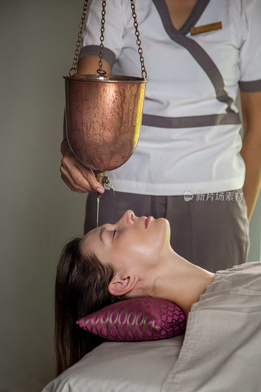 Shirodhara，一种阿育吠陀治疗技术。女性前额滴油。一名年轻女子的肖像在阿育吠陀按摩会议与芳香油滴在她的前额和头发。