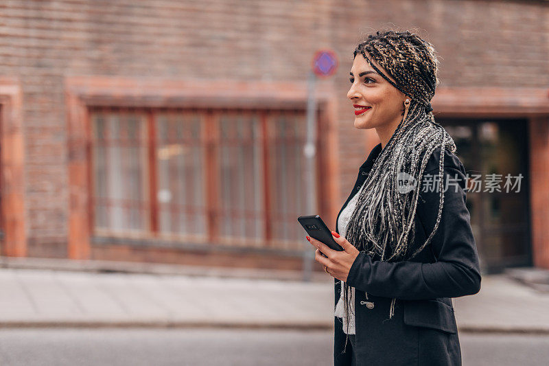 美丽的女人站在街上玩智能手机