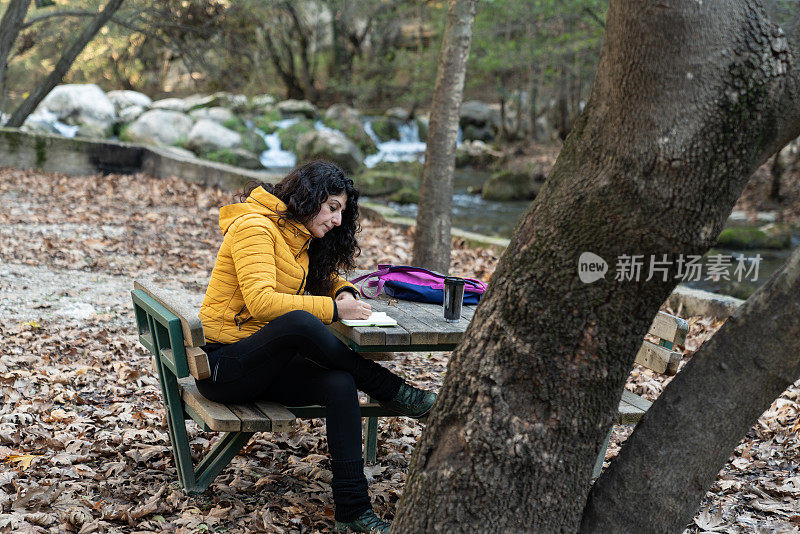 成年妇女坐在公园长椅上写秋天的季节