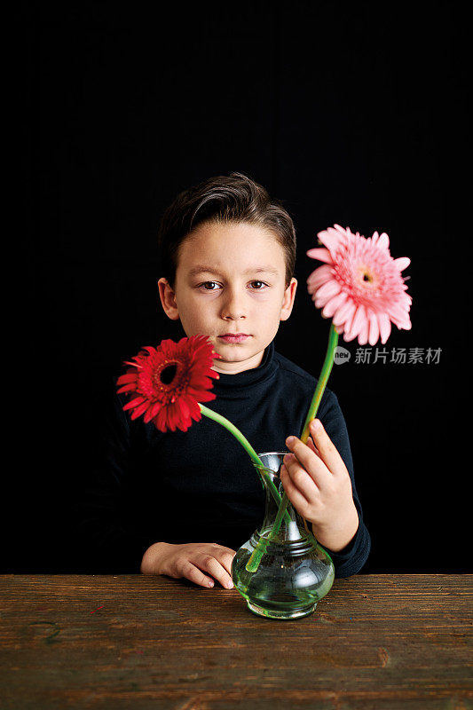 6-7岁的可爱的孩子坐在桌子上，彩色的花朵在黑色的背景。