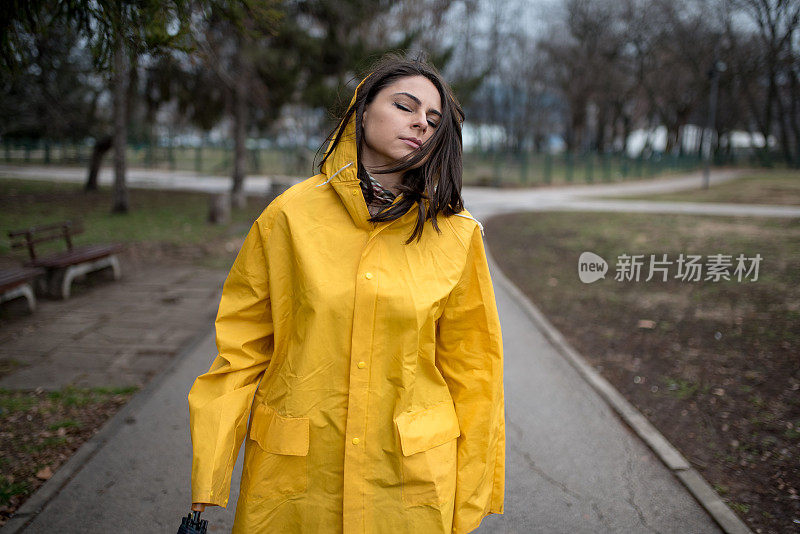 穿着黄色雨衣的年轻女子在公园里度过雨天