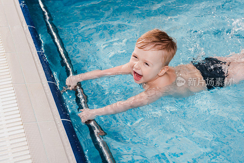 头顶视图兴奋的蹒跚学步的男孩游泳附近的扑板在游泳池