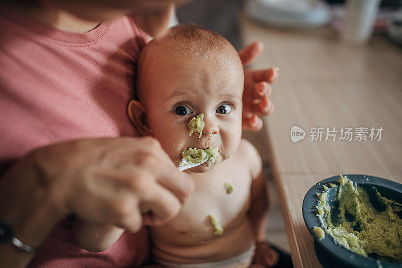 年轻的母亲试图用勺子喂一个调皮的婴儿
