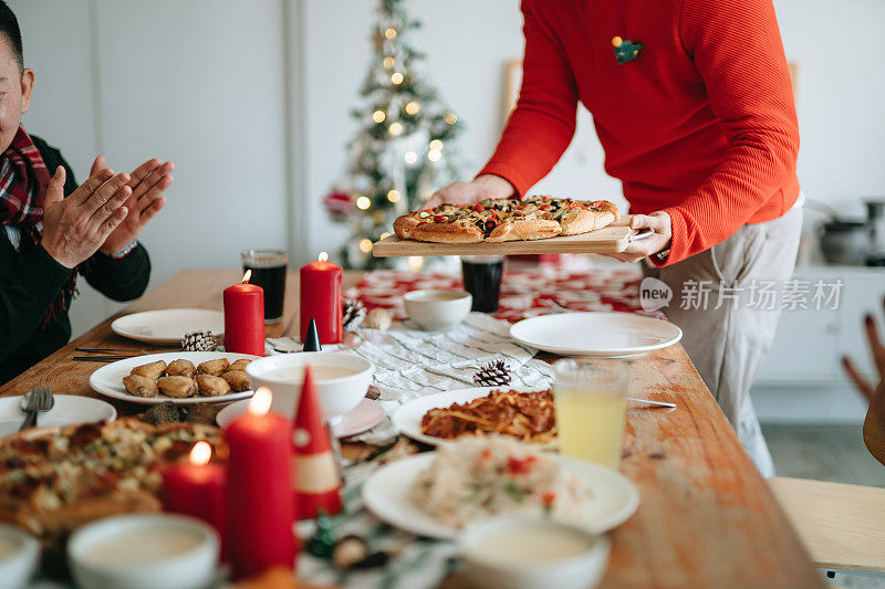 快乐的亚洲多代家庭花时间一起庆祝圣诞节，微笑的年轻人在圣诞派对期间在家里为家人服务食物