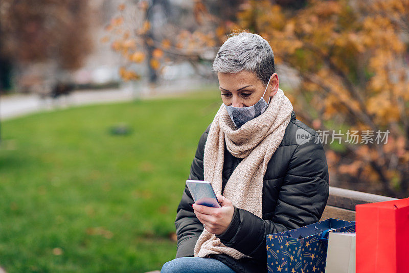 买完圣诞礼物后，带口罩的女人正在用智能手机休息