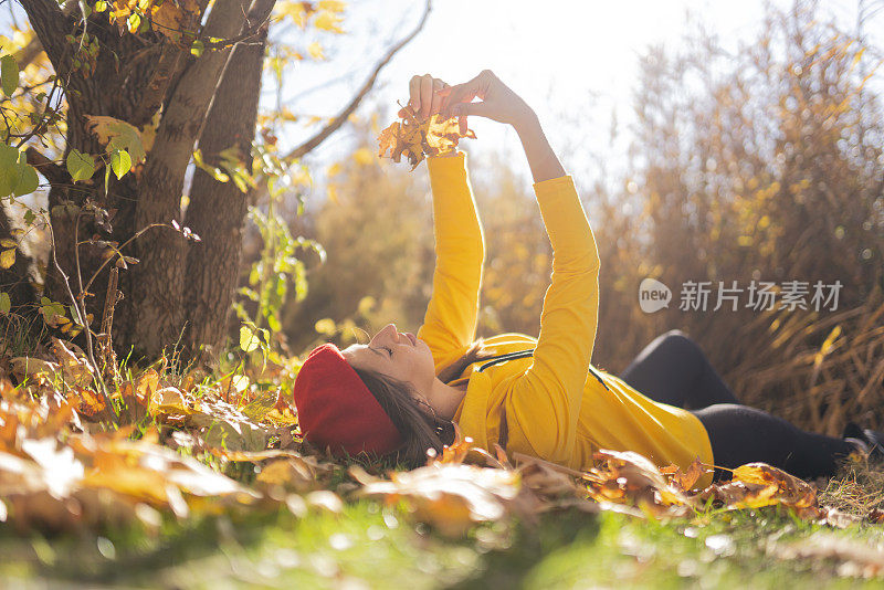 季节和人的概念-肖像美丽的年轻女子躺在地上的秋天森林与五颜六色的枫叶。