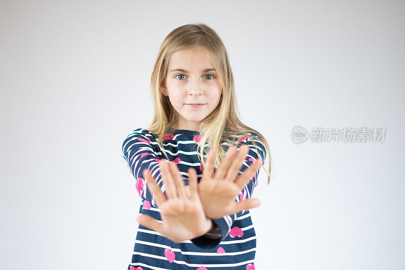 小女孩在白色的背景下做着手心停止唱歌。警告表情与否定和严肃的手势在脸上。