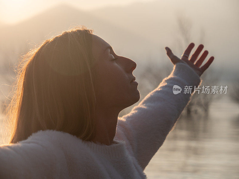 女人拥抱自然，她在夕阳西下的湖边伸出双臂