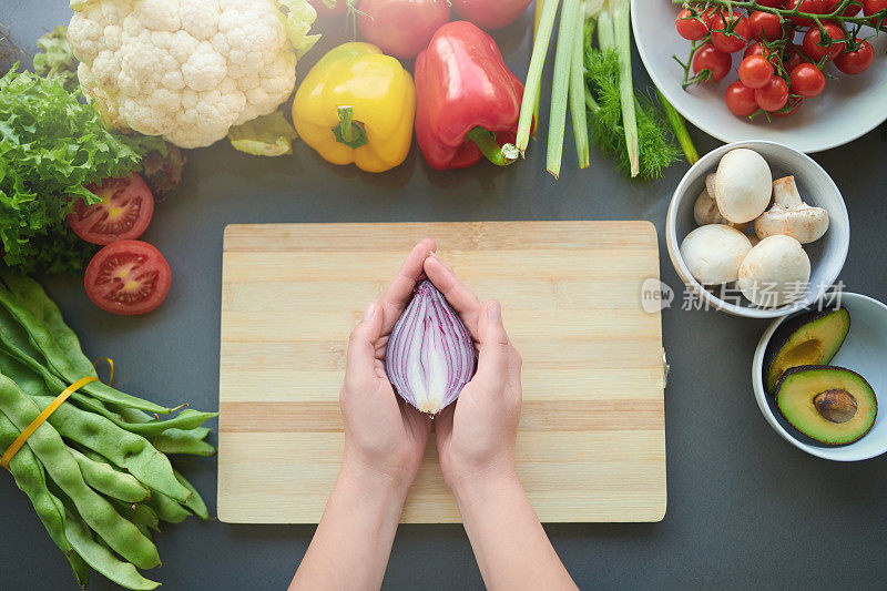 照片中，一位面目全非的妇女拿着一片洋葱，在家准备一顿健康餐