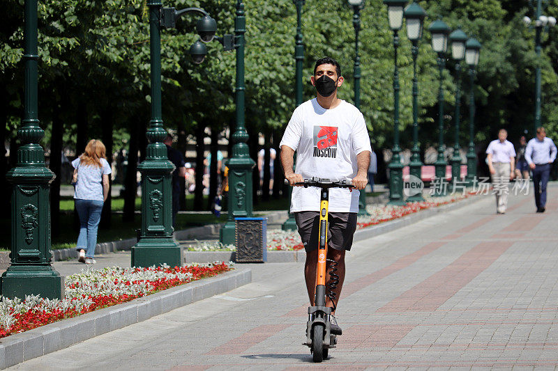 在夏天的城市里，一个戴着保护面罩的人骑着电动车