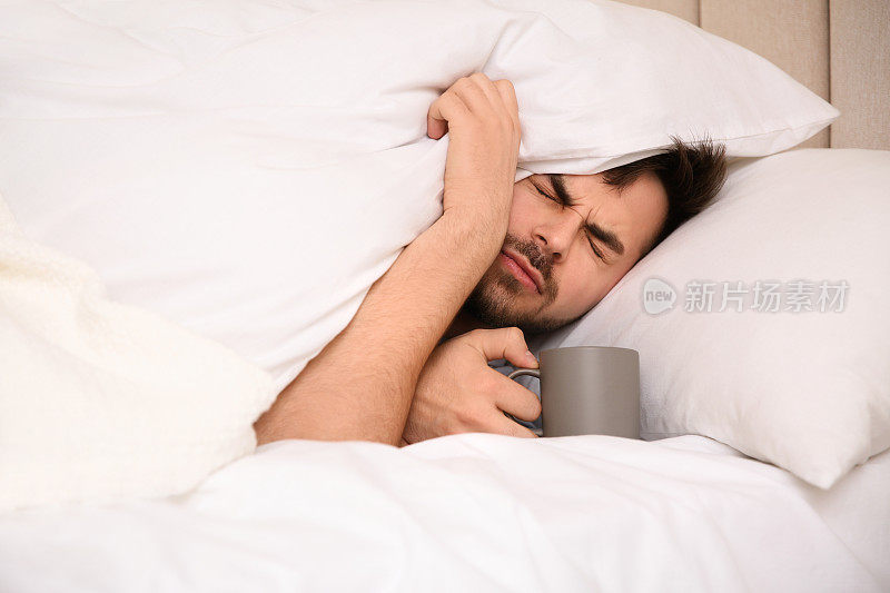 生病的年轻人在家里的床上喝着一杯热饮。流感病毒
