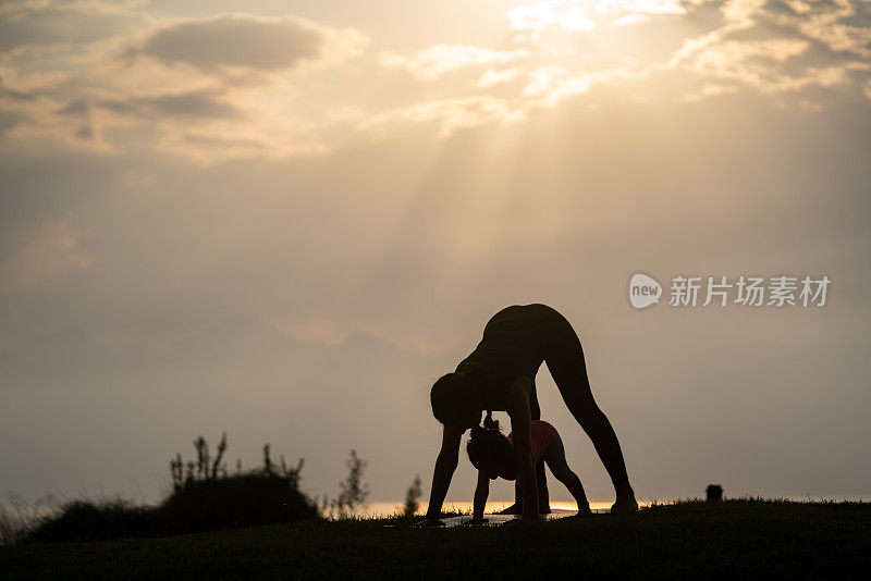 成年妇女和小女孩在夕阳下做瑜伽练习的剪影