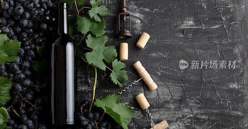 红酒酒瓶葡萄串与叶子和藤蔓开塞钻深色乡村混凝土背景。在黑色的石头桌子上平放红酒组合瓶。长网页横幅与复制空间。