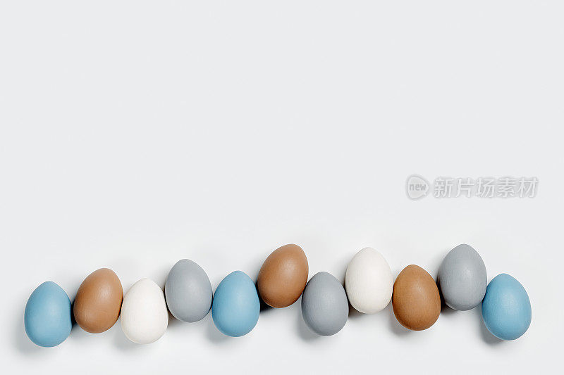 染色复活节蛋柔和的颜色蓝色，灰色，米色在白色的背景行。复活节节日快乐，庆祝美食理念，鸡蛋中性新潮色彩。顶视图表