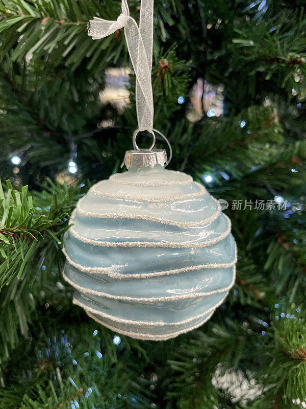 个人的形象，蓝色的肋小装饰物挂在人造圣诞树的树枝上，云杉针，模糊的白色仙女光的背景