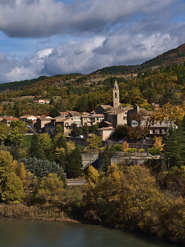 法国普罗旺斯市Sisteron镇的一个小村庄，教堂和传统建筑的美丽景色，在秋天被五颜六色的树木环绕，杜兰斯河在前面。