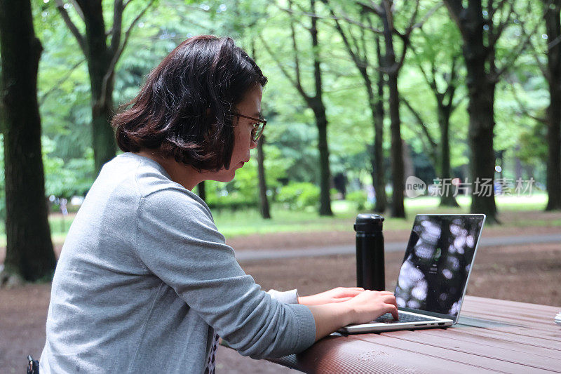 一个年轻女子坐在公园的户外，手里拿着一台笔记本电脑